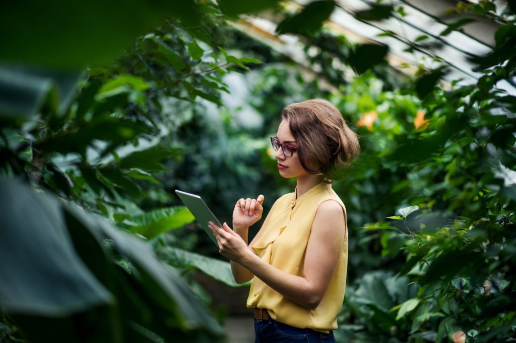 Young woman standing in greenhouse in botanical garden, using tablet